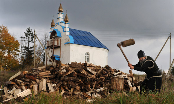 Священник рубит драва возле церкви в деревне