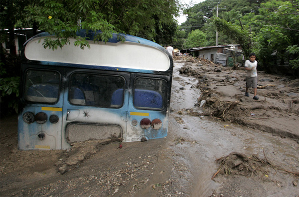 Сальвадорский мальчик идет возле полузатопленного в грязи автобуса