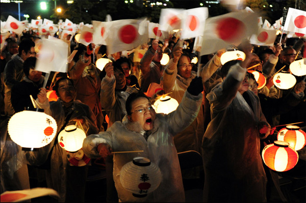 Люди машут японскими флагами и держат фонари, стоя перед императорским дворцом в Токио во время празднования 20-летия коронации Императора Акихито