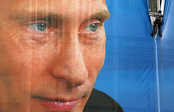 Рабочий снимает плакат с изображением Владимира Путина после выборов в Москве